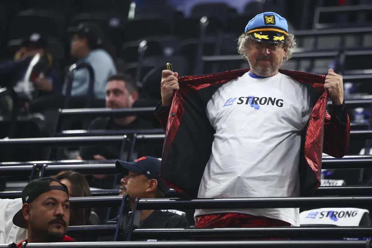 مشجع يرتدي قميصًا مكتوبًا عليه \"LA STRONG\" ويظهر بفخر في مدرجات مباراة كليبرز وميامي هيت، مع تواجد مشجعين آخرين في الخلفية.