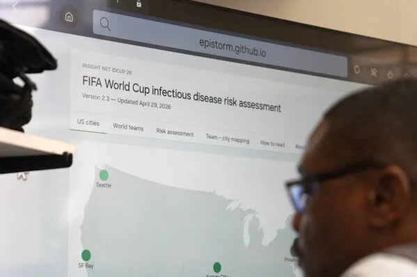 شخص يتابع شاشة تعرض خريطة تقييم مخاطر الأمراض المعدية خلال كأس العالم، مع التركيز على المدن الأمريكية المستضيفة.