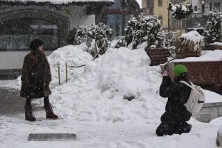 امرأة ترتدي ملابس شتوية تقف في الثلوج بينما يقوم مصور يرتدي قبعة خضراء بالتقاط صور لها في كورتينا دامبيزو، إيطاليا.