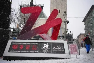 شعار دورة الألعاب الأولمبية الشتوية 2026 في كورتينا دامبيزو، محاط بالثلوج، مع عداد تنازلي يظهر الوقت المتبقي حتى انطلاق الألعاب.