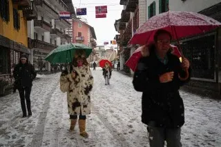 مشاة يحملون مظلات في شوارع كورتينا دامبيزو المغطاة بالثلوج، مع تساقط الثلوج المستمر في المدينة استعدادًا لألعاب ميلانو كورتينا.