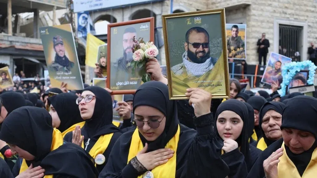 محتجون يرتدون الأسود ويحتفلون بذكرى أحد أفراد حزب الله، يحملون صورًا له، مع أجواء من الحزن والاحترام.