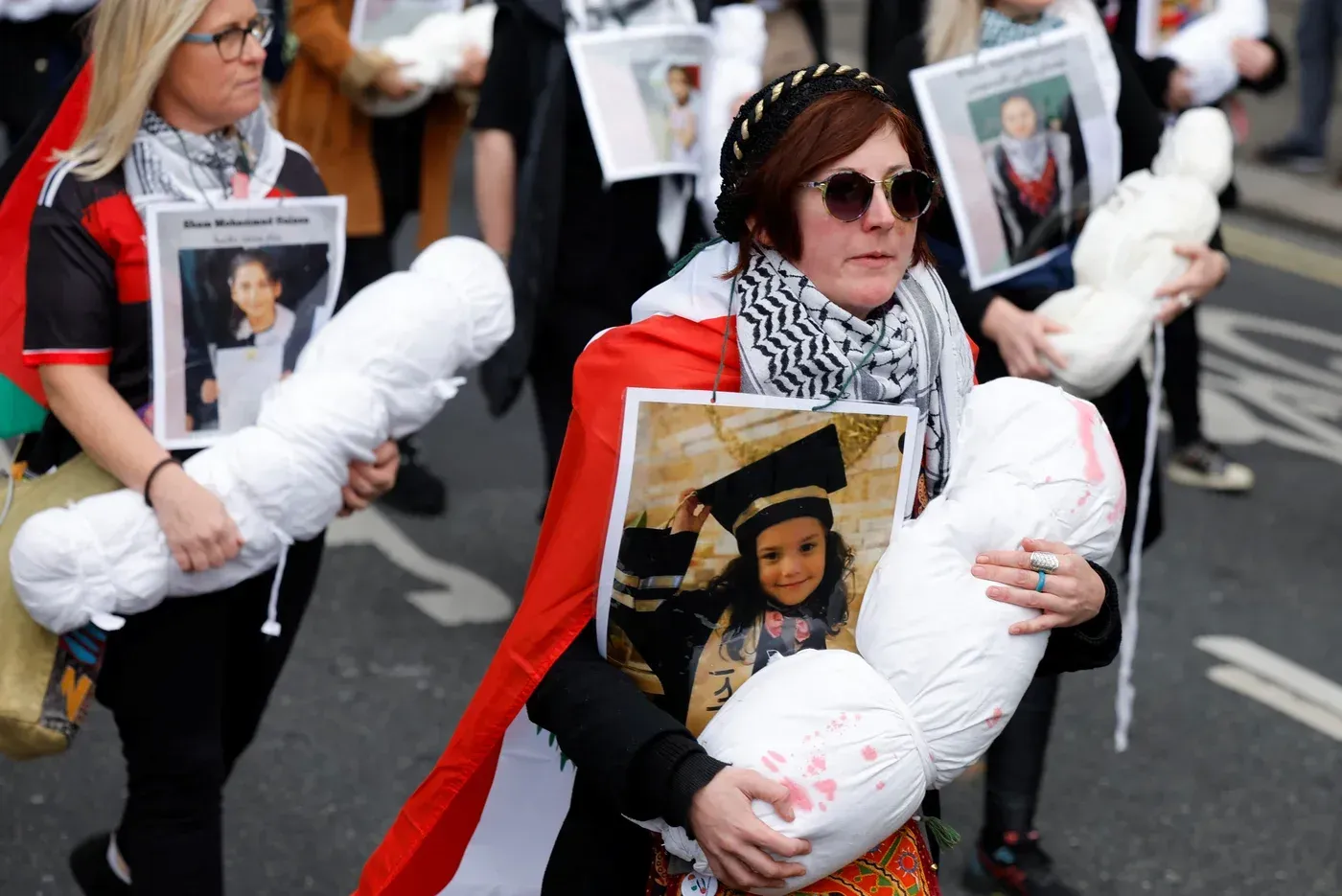 نساء يحملن دمى تمثل أطفالاً في مظاهرة، يرتدين الزي الفلسطيني، وملصقات تحمل صور هند رجب.
