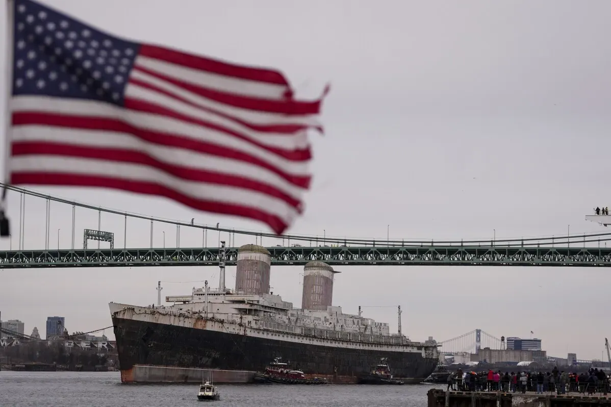 سفينة SS United States التاريخية تبحر من نهر ديلاوير، مع العلم الأمريكي في المقدمة، استعدادًا لتحويلها إلى شعاب مرجانية اصطناعية في فلوريدا.