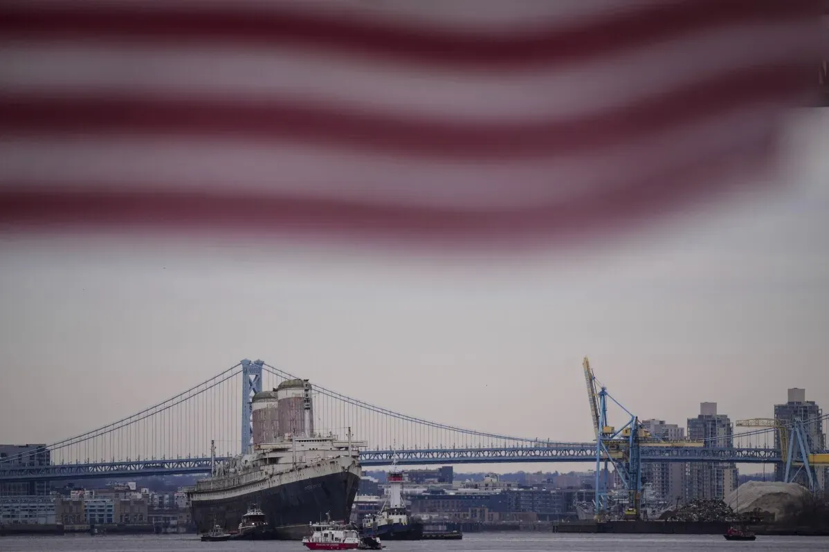 سفينة SS United States التاريخية تبحر من نهر ديلاوير، مع جسر خلفي، في بداية رحلتها لتحويلها إلى شعاب مرجانية اصطناعية في فلوريدا.