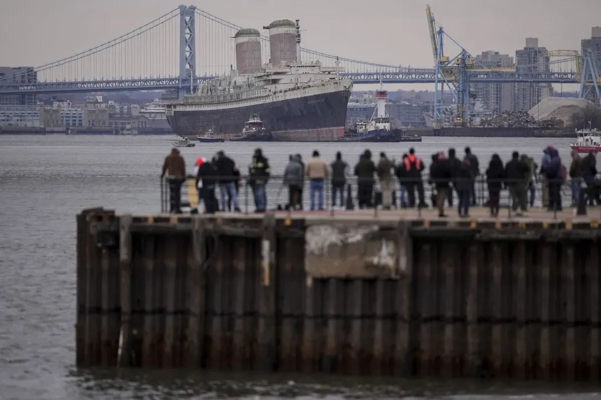 سفينة SS United States التاريخية تبحر من واجهة نهر ديلاوير، بينما يشاهدها حشد من الناس، استعدادًا لتحويلها إلى شعاب مرجانية اصطناعية في فلوريدا.