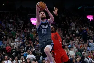 لاعب يوتا يسجل نقطة خلال مباراة ضد بورتلاند، مع وجود مدافع من الفريق المنافس في الخلفية، وسط جمهور متحمس.