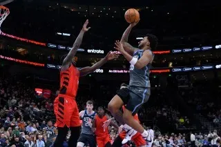 لاعب يوتا يسجل سلة بينما يحاول مدافع بورتلاند اعتراضه، وسط أجواء حماسية في مباراة كرة السلة.