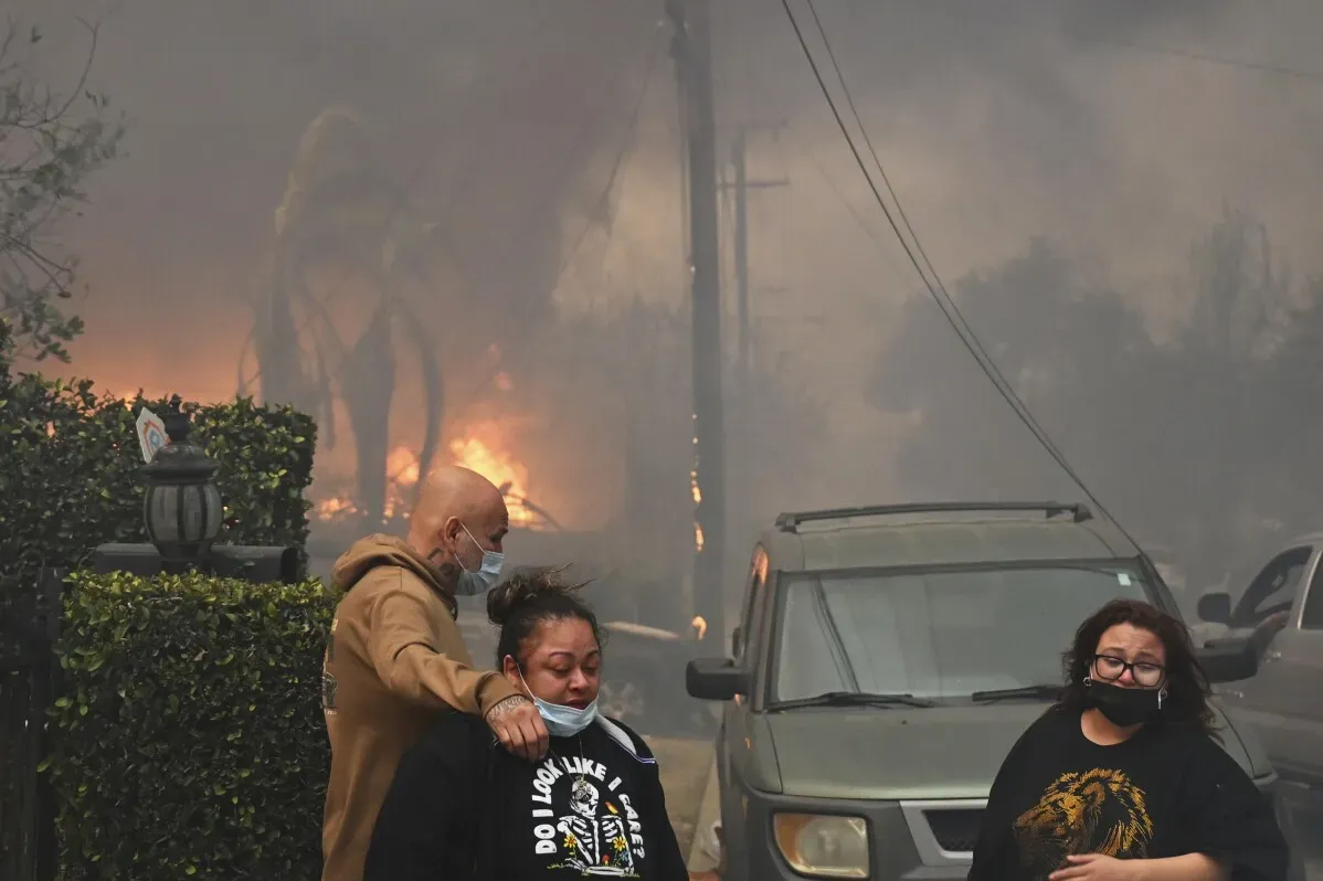 سكان يهربون من حرائق هوليوود، مع ألسنة اللهب والدخان في الخلفية، وسط أجواء من الفوضى والقلق في المنطقة.