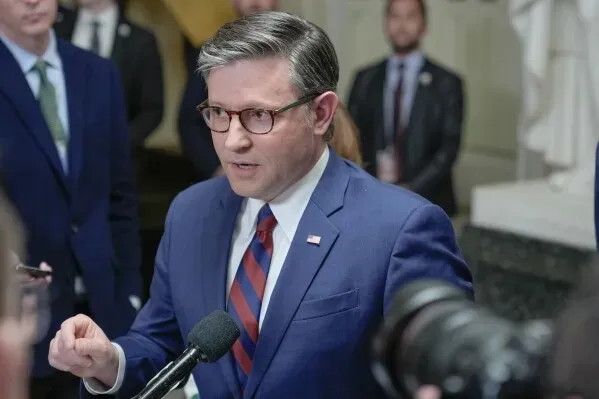 رجل يرتدي بدلة زرقاء يتحدث أمام ميكروفون، مع وجود أشخاص آخرين في الخلفية، خلال مؤتمر صحفي حول تمويل وزارة الأمن الداخلي.