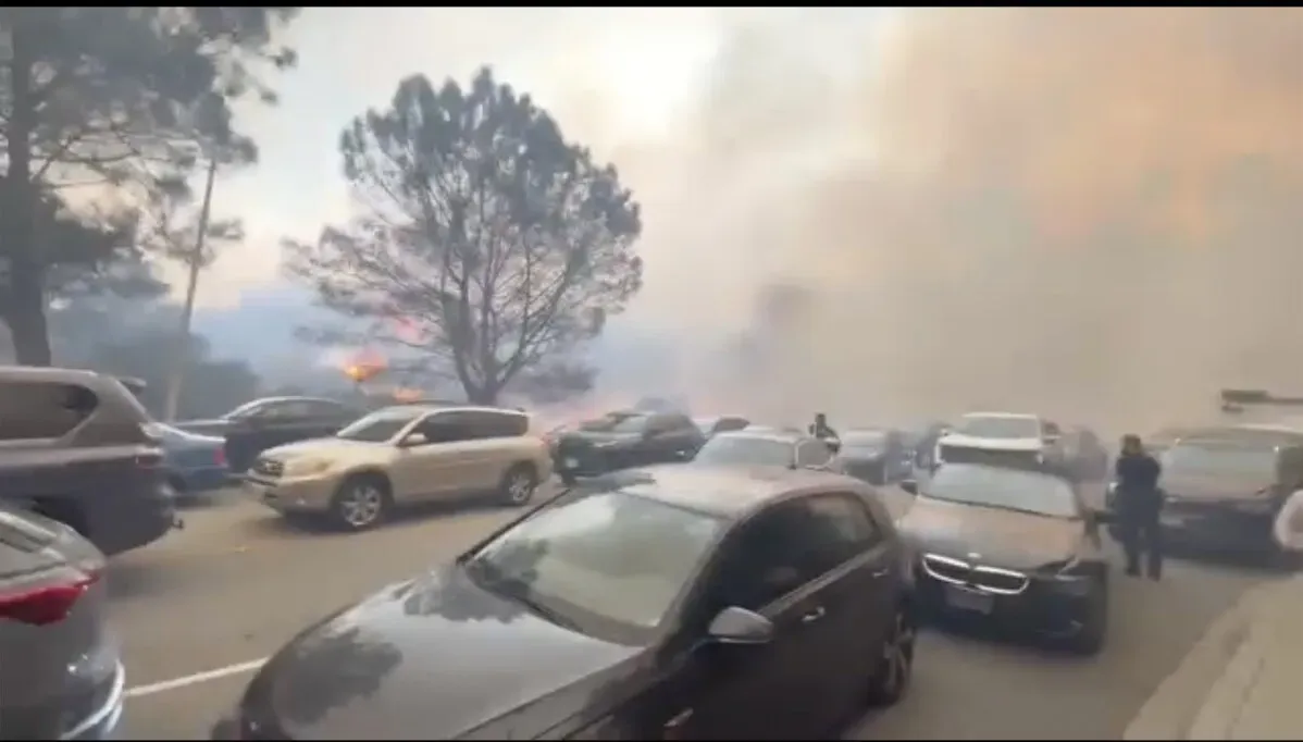 ازدحام مروري بسبب حرائق غابات باسيفيك باليساديس، مع دخان كثيف يتصاعد وأشخاص يحاولون مغادرة سياراتهم في حالة من القلق.