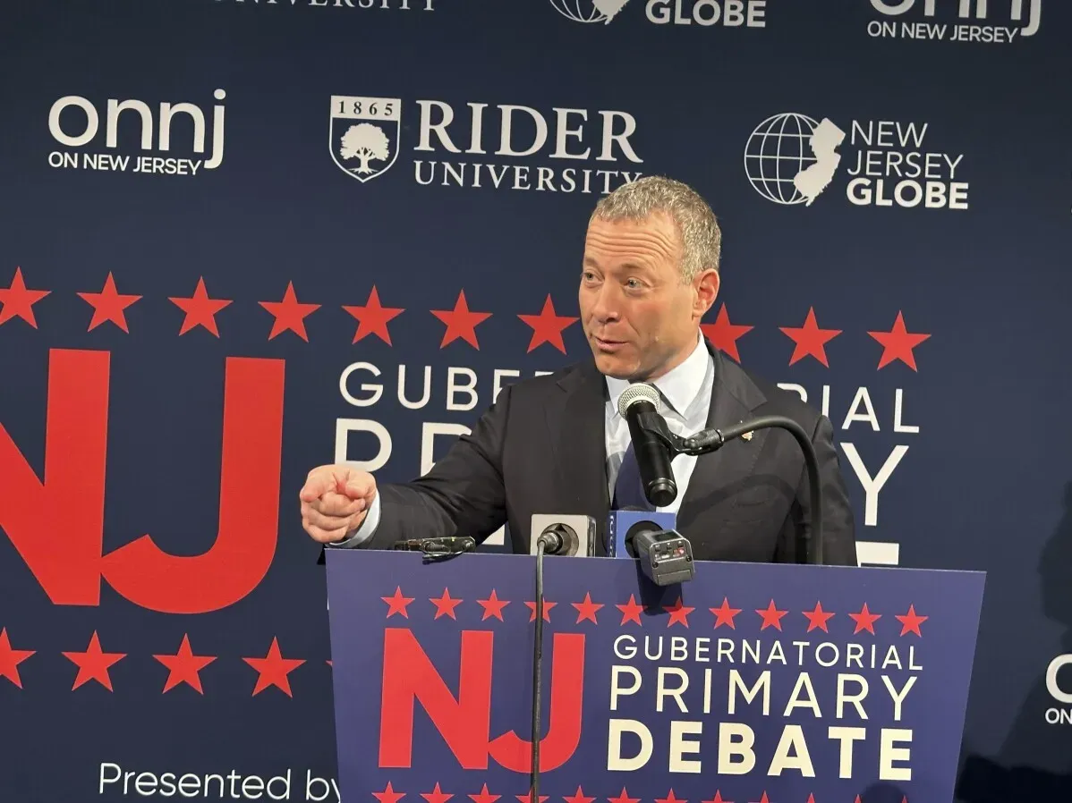 النائب جوش غوتهايمر يتحدث في مناظرة انتخابية، مع خلفية تحمل شعار "NJ Gubernatorial Primary Debate" في جامعة رايدر.