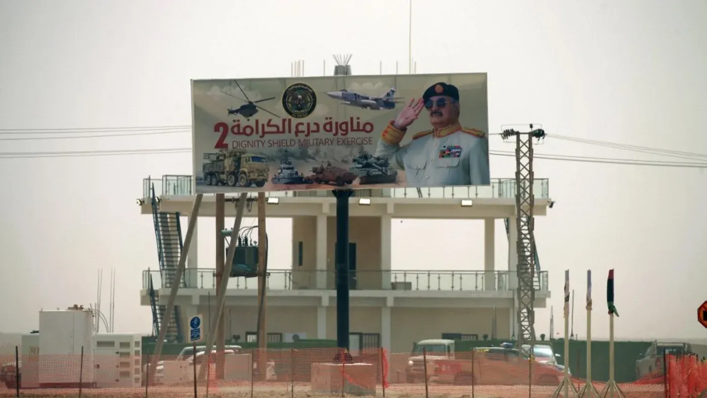 لافتة إعلانية كبيرة تُظهر صورة عسكرية مع نص عربي يشير إلى "درع الكرامة 2"، تعكس الأجواء العسكرية في ليبيا.