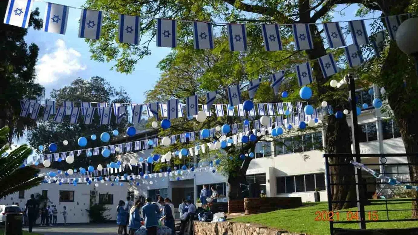 ساحة مدرسة روديان الثانوية للبنات مزينة بأعلام إسرائيلية وزينة باللونين الأزرق والأبيض، مع تجمعات للطلاب في الخلفية.