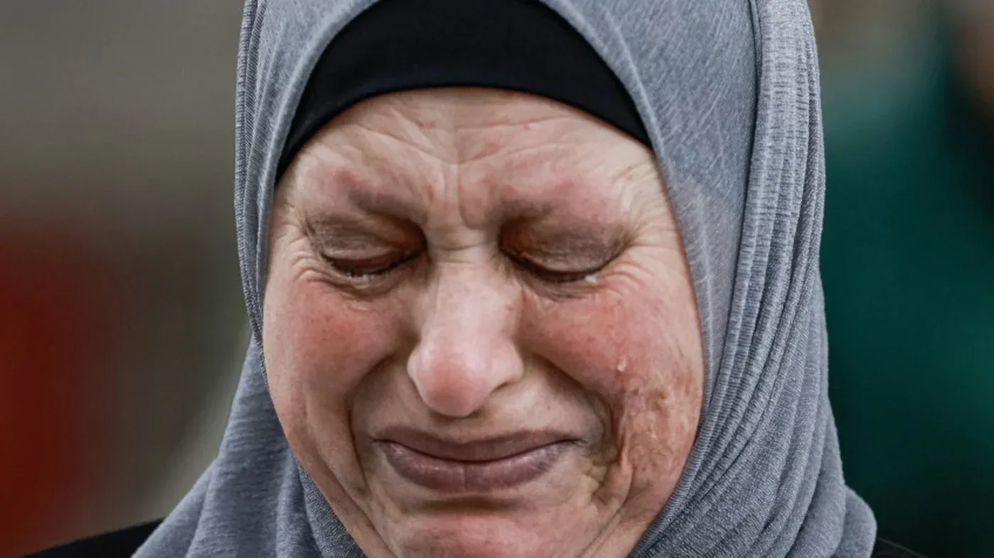 امرأة ترتدي الحجاب، تعبر عن حزن عميق، مع دموع تتدفق على وجهها، تعكس مشاعر الألم والمعاناة في سياق الأحداث المؤلمة المذكورة في المقال.