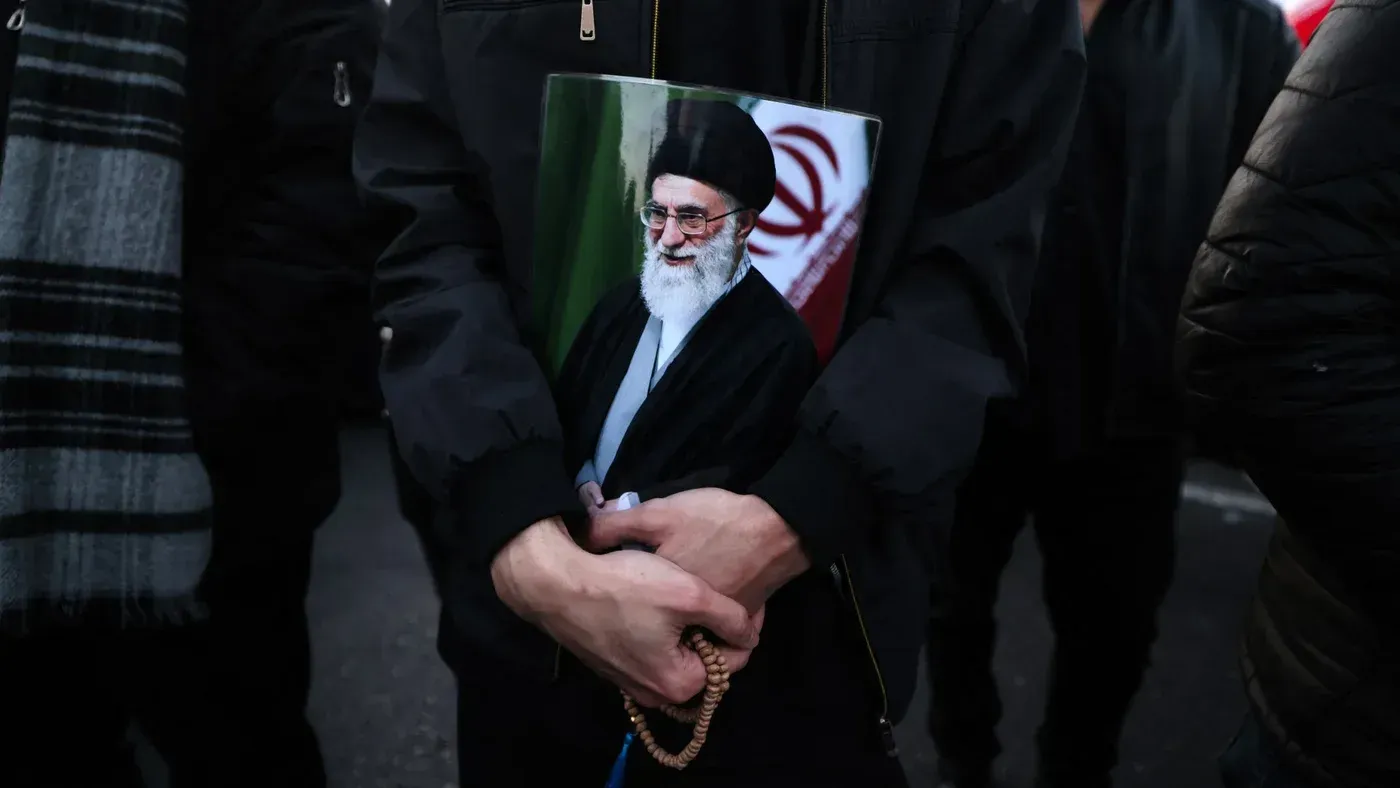 رجل يحمل صورة لآية الله علي خامنئي وسط حشود في طهران، معبرة عن مشاعر مختلطة من الحزن والاحتفال بعد وفاته.