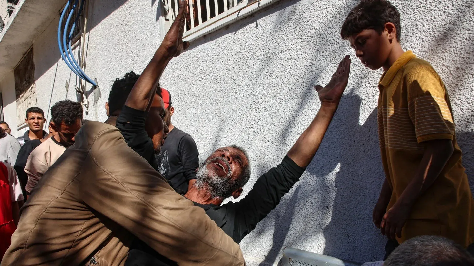 رجل مسن يُعبر عن حزنه وسط مجموعة من الرجال والشبان في غزة، في مشهد يعكس معاناة المدنيين خلال الحرب.