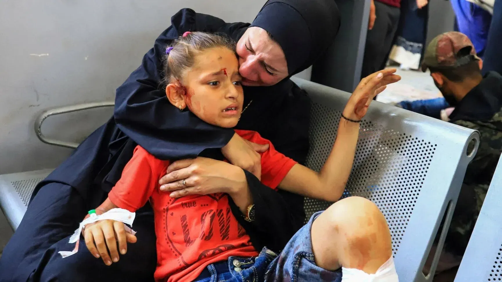 امرأة تحتضن طفلًا مصابًا في مستشفى، حيث تظهر علامات الألم والقلق على وجههما، في ظل الظروف الصعبة في غزة.