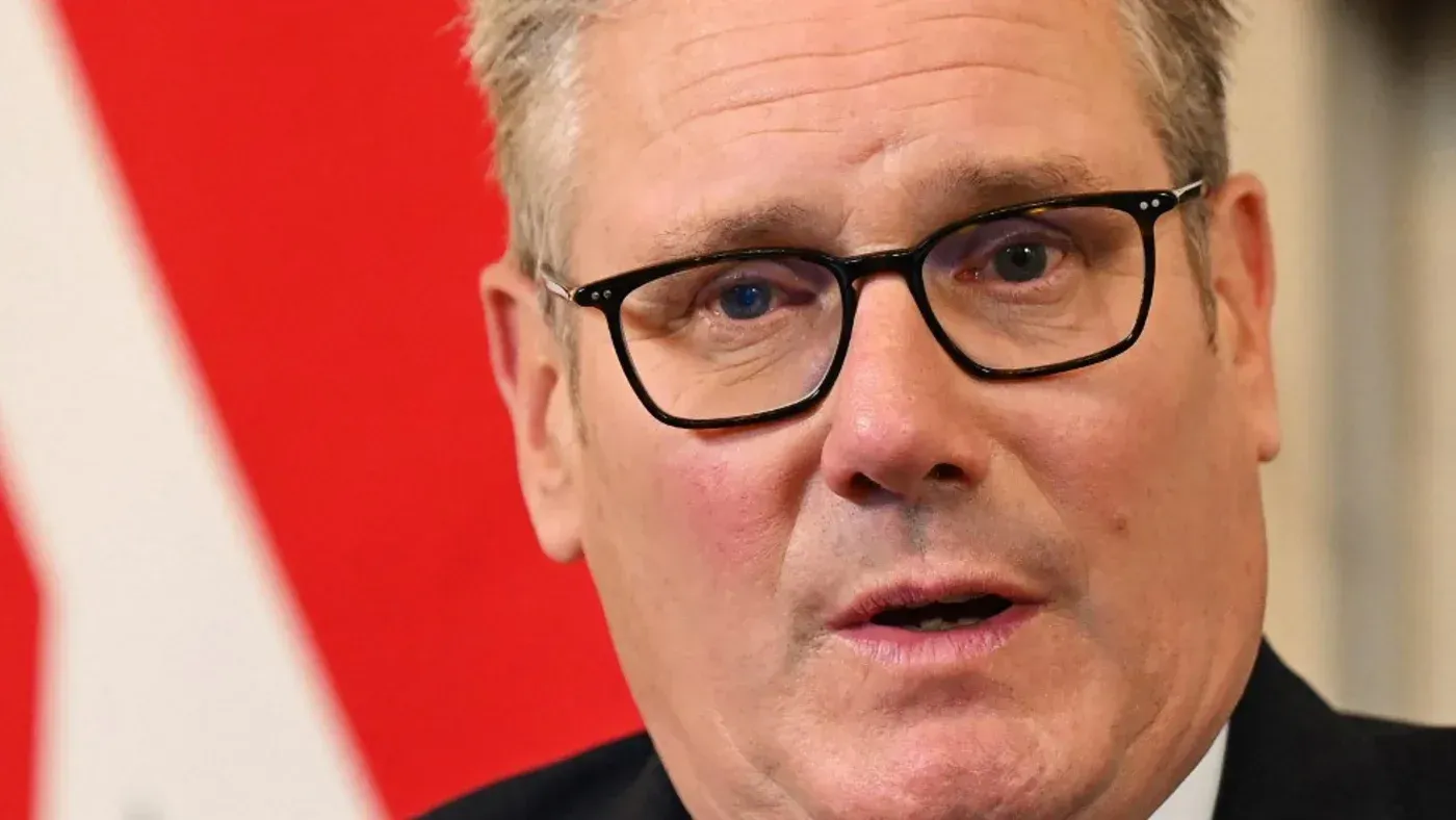 صورة مقربة لكير ستارمر، زعيم حزب العمال البريطاني، يظهر فيها تعبيره الجدي وسط خلفية حمراء، تعكس الضغوط السياسية الناتجة عن فضيحة إبشتاين.