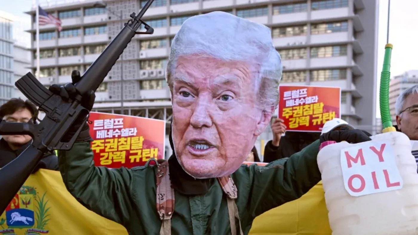 شخص يرتدي قناعًا كبيرًا لرئيس ترامب ويحمل سلاحًا، مع لافتة مكتوب عليها "نفطي"، في سياق احتجاجات ضد سياساته.