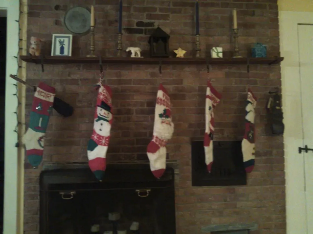جوارب عيد الميلاد المحبوكة يدويًا معلقة على رف فوق المدفأة، تشكل تذكيرًا بالذكريات العائلية والاحتفالات التقليدية.