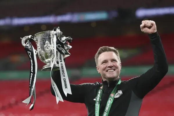 إيدي هاو مدرب نيوكاسل يحتفل بفوزه بكأس، بينما يحمل الكأس في يده وسط أجواء احتفالية في الملعب.