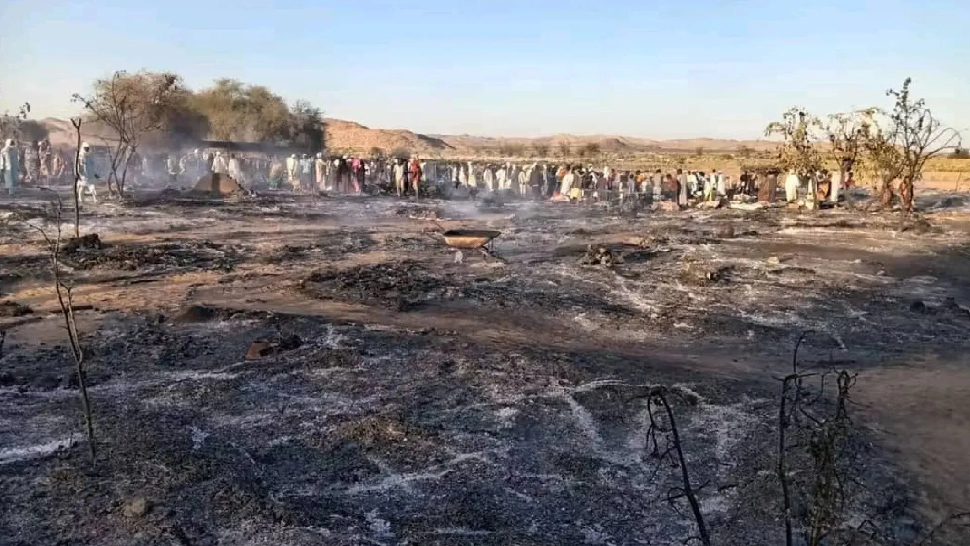 مشهد يظهر أنقاض سوق طرة في غرب دارفور بعد الهجوم، مع تجمع عدد من الأشخاص في الخلفية وسط الدخان والخرائب.