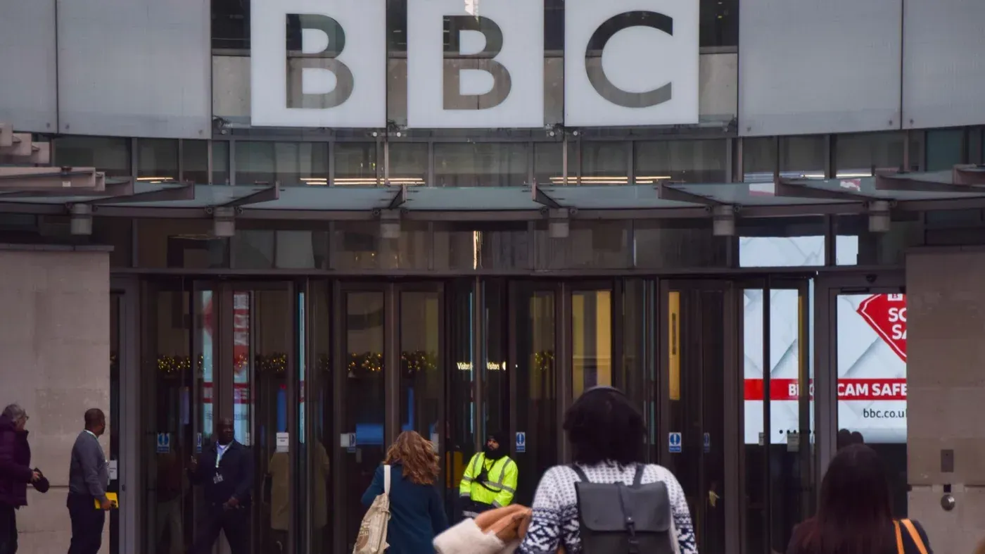 مدخل مبنى بي بي سي، حيث يظهر عدد من الأشخاص يتجهون نحو المدخل، مع لافتة واضحة تحمل شعار المؤسسة الإعلامية.