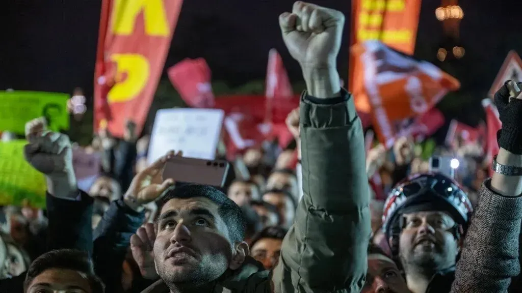 تظهر الصورة مجموعة من المتظاهرين في إسطنبول يرفعون قبضاتهم ويهتفون، تعبيرًا عن احتجاجهم على اعتقال رئيس البلدية أكرم إمام أوغلو.