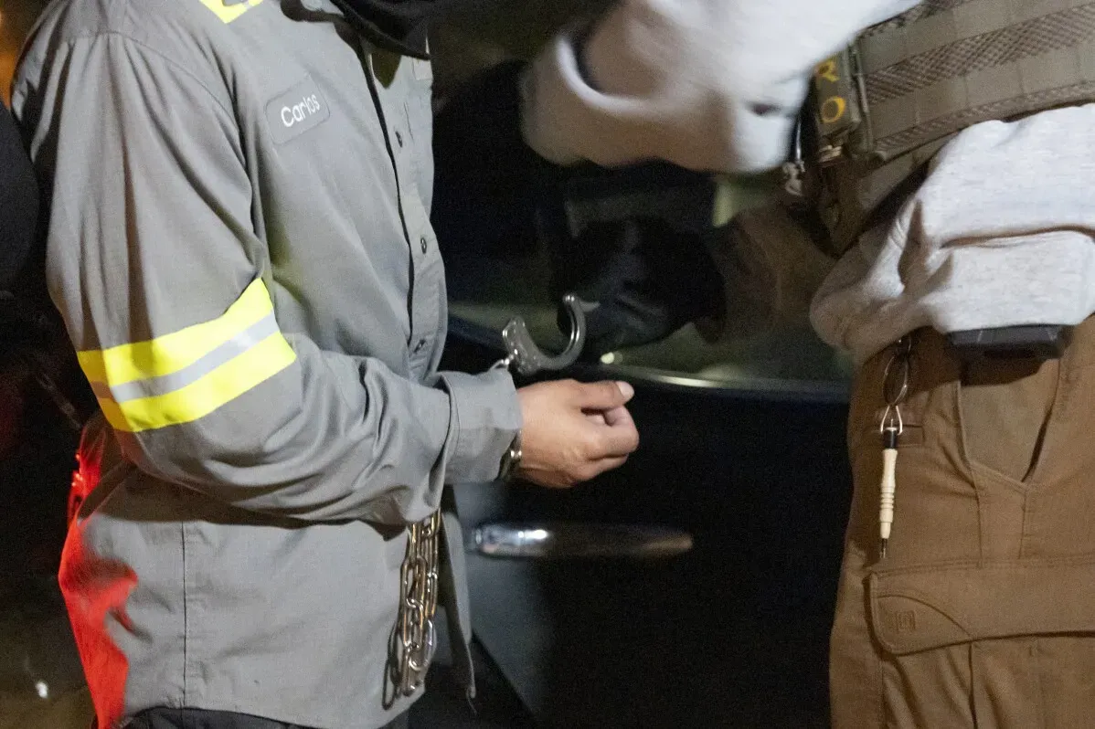 تظهر الصورة ضابط إنفاذ قوانين الهجرة والجمارك وهو يعتقل شخصًا يحمل سلاسل، مما يعكس العمليات المتزايدة لترحيل المهاجرين غير الشرعيين في الولايات المتحدة.