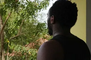 رجل أفريقي يقف في مكان مفتوح، ينظر إلى الأشجار من خلفه، معبرًا عن مشاعر القلق بعد هروبه من مجمع احتيال في كمبوديا.