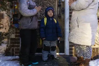 أطفال يرتدون ملابس شتوية ينتظرون أمام باب منزلهم في مينيابوليس، بينما تصلي والدتهم من أجل سلامتهم في ظل مخاوف الهجرة.