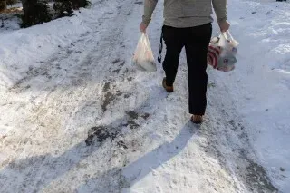 شخص يحمل أكياسًا في يديه أثناء المشي على طريق مغطى بالثلوج، يعكس تحديات الحياة اليومية للعائلات المهاجرة في مينيابوليس.