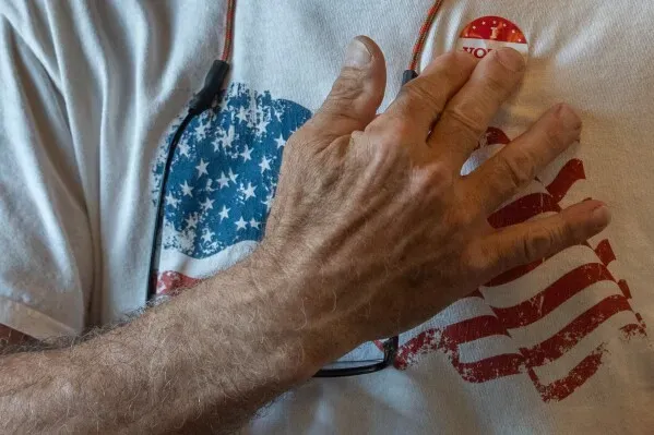 رجل يرتدي قميصًا مزينًا بعلم الولايات المتحدة، يضع يده على زر "صوت" في سياق الانتخابات في فيرجينيا.