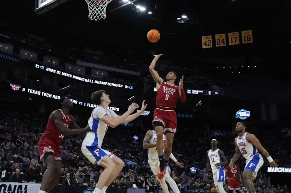 لاعب كرة سلة يقوم بتسديدة عائمة نحو السلة، وسط لاعبين آخرين في مباراة بطولة NCAA، مع التركيز على تقنيات التسديد.