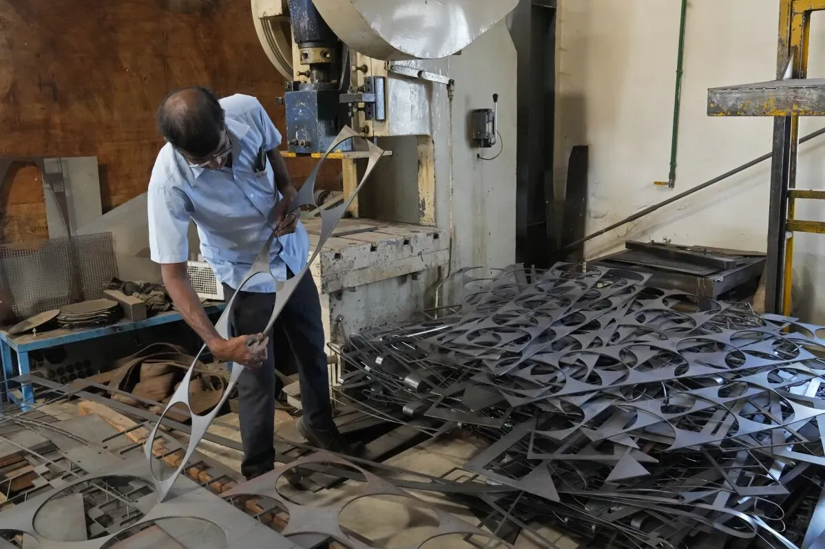 عامل في مصنع للصلب في بنغالورو، يقوم بتشكيل قطع معدنية من الفولاذ، وسط كومة من المواد المعدنية المعالجة.