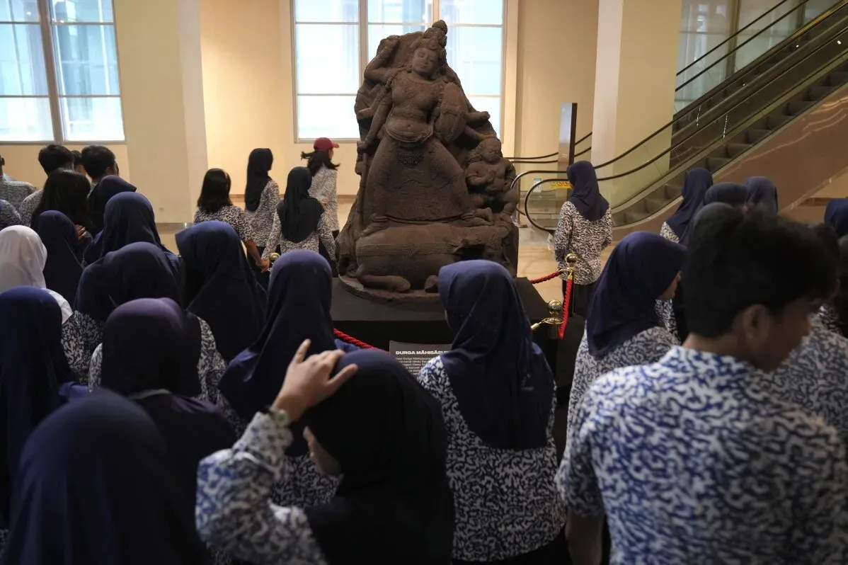 مجموعة من الطلاب يرتدون زيًا موحدًا، يواجهون تمثالًا حجريًا لبوذا في المتحف الوطني الإندونيسي، حيث تم إعادة القطع الأثرية من هولندا.