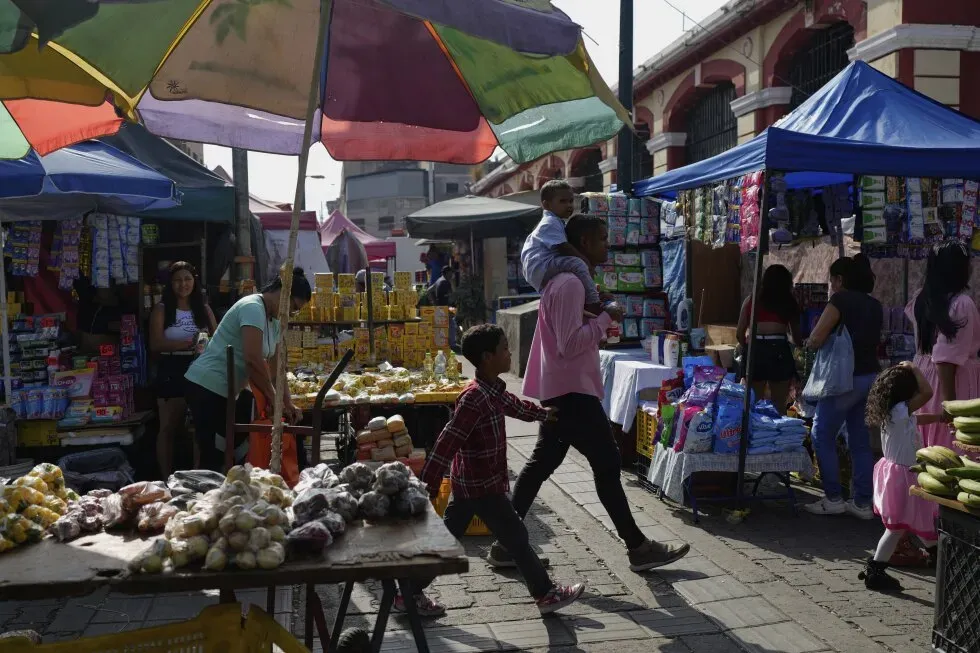 سوق مزدحم في ماراكايبو، فنزويلا، حيث يتسوق الناس بين أكشاك بيع المواد الغذائية والسلع الأساسية تحت مظلات ملونة.