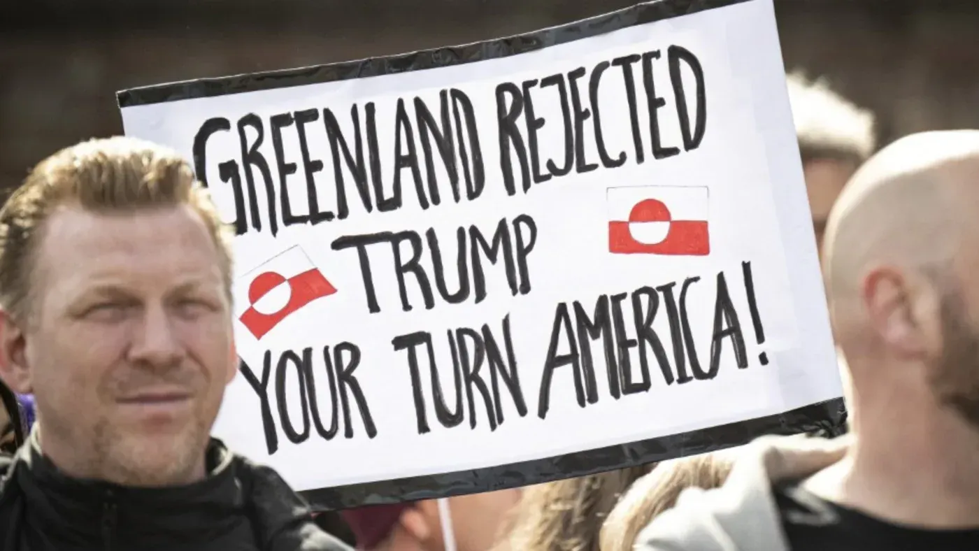 لافتة في مظاهرة تحمل عبارة "غرينلاند رفضت ترامب، دورك يا أمريكا!" مع علم غرينلاند، تعبر عن رفض التدخل الأمريكي.