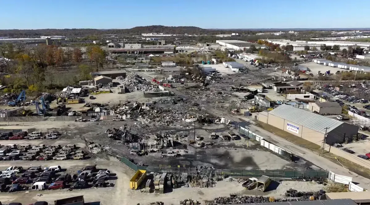 موقع تحطم طائرة شحن UPS في لويزفيل، حيث تظهر آثار الحريق والدمار في المنطقة، مع وجود سيارات متضررة في الخلفية.