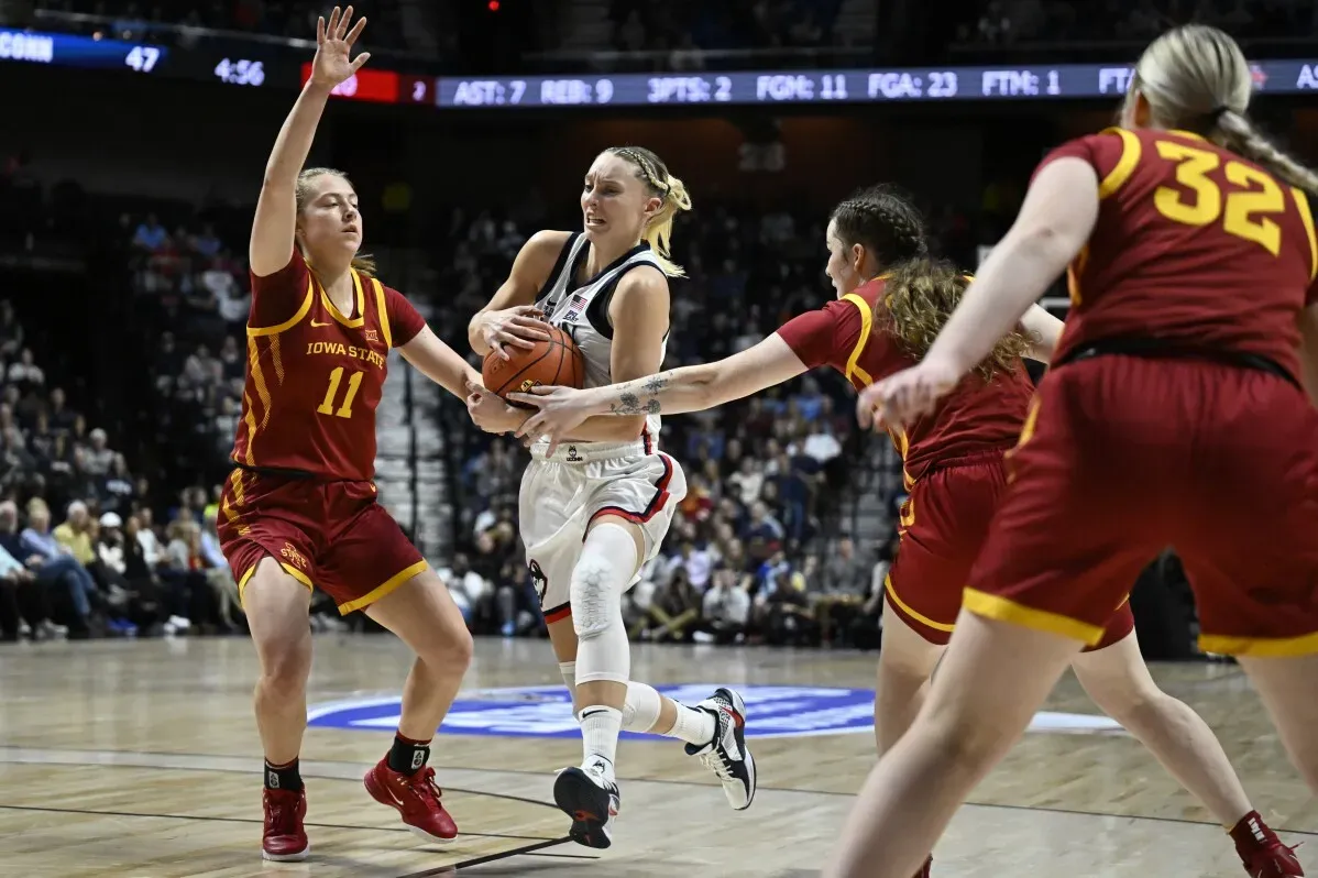 لاعبة كرة سلة تتعرض لضغط من لاعبتين من فريق ولاية آيوا خلال مباراة NCAA، مع التركيز على المنافسة الشديدة.