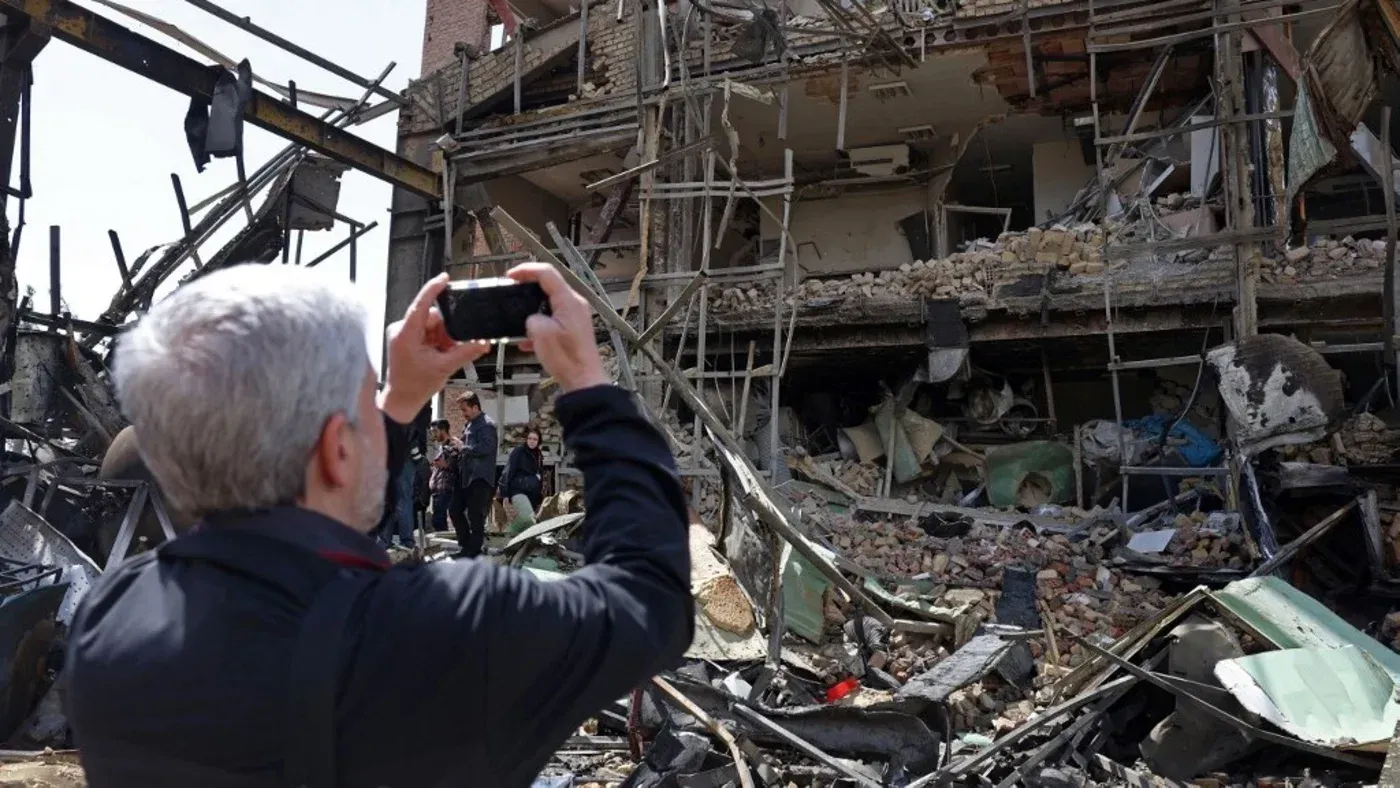 رجل يلتقط صورة لهدم مبنى متضرر، مع ظهور حطام وبقايا مواد بناء، في سياق الأحداث العسكرية الأخيرة في إيران.