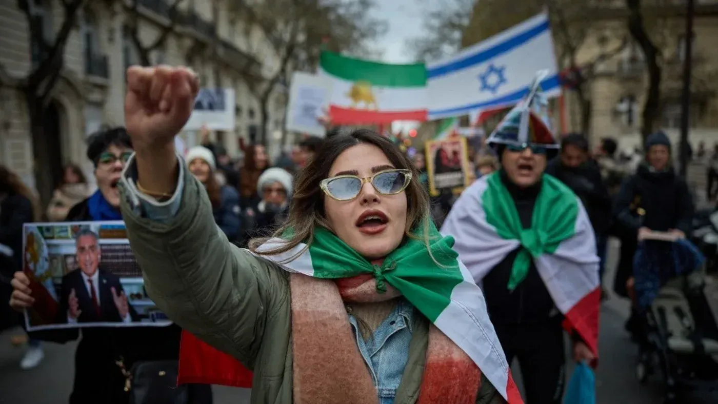 متظاهرة ترتدي نظارات شمسية وتحمل علم إيران، تعبر عن احتجاجها في تظاهرة ضد الحكومة، وسط حشود من المتظاهرين.