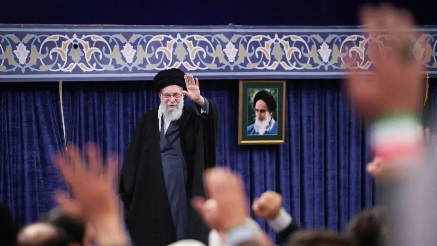المرشد الأعلى علي خامنئي يلوح بيده خلال تجمع، مع صورة خلفية له، في سياق التوترات حول البرنامج النووي الإيراني والمفاوضات مع الولايات المتحدة.
