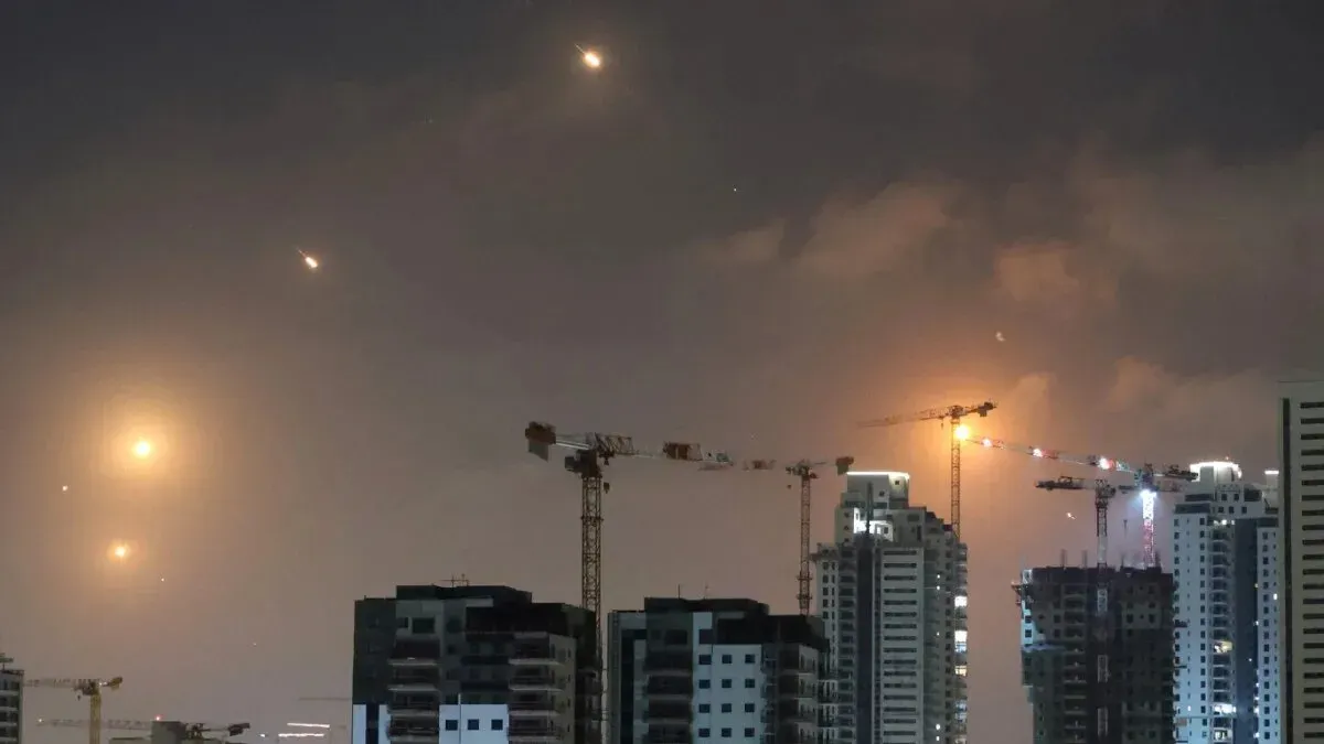 سماء تل أبيب مضاءة بأضواء برتقالية نتيجة إطلاق صواريخ من إيران، مع ظهور حرائق ودخان في المدينة.
