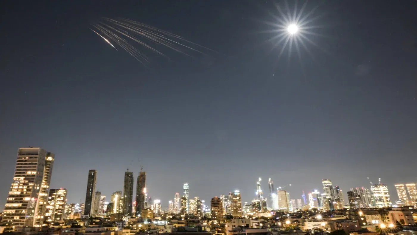صواريخ تتجه نحو السماء فوق مدينة مضاءة ليلاً، مع ظهور القمر في الخلفية، تعكس التوترات العسكرية في الشرق الأوسط.