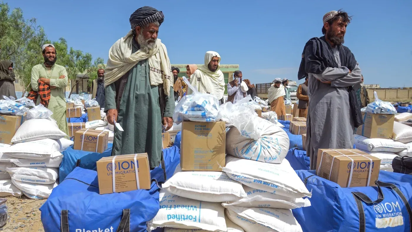 تجمع رجال أفغان في موقع توزيع المساعدات الإنسانية، محاطين بأكياس تحتوي على إمدادات غذائية ومواد ضرورية، وسط أزمة إنسانية متفاقمة.