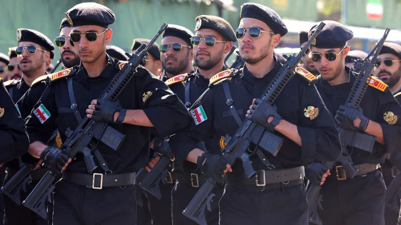 جنود إيرانيون يرتدون زيًا عسكريًا ويحملون أسلحة خلال عرض عسكري، مع التركيز على استعدادهم الدفاعي وسط التوترات الإقليمية.