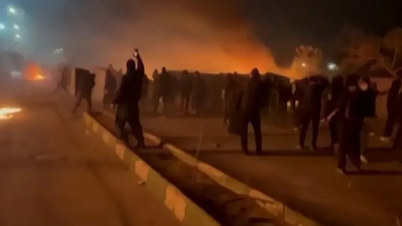 مظاهرة في إيران ليلاً، حيث يتجمع المحتجون في مواجهة النيران والدخان، مع تصاعد التوترات بسبب القضايا الاقتصادية.