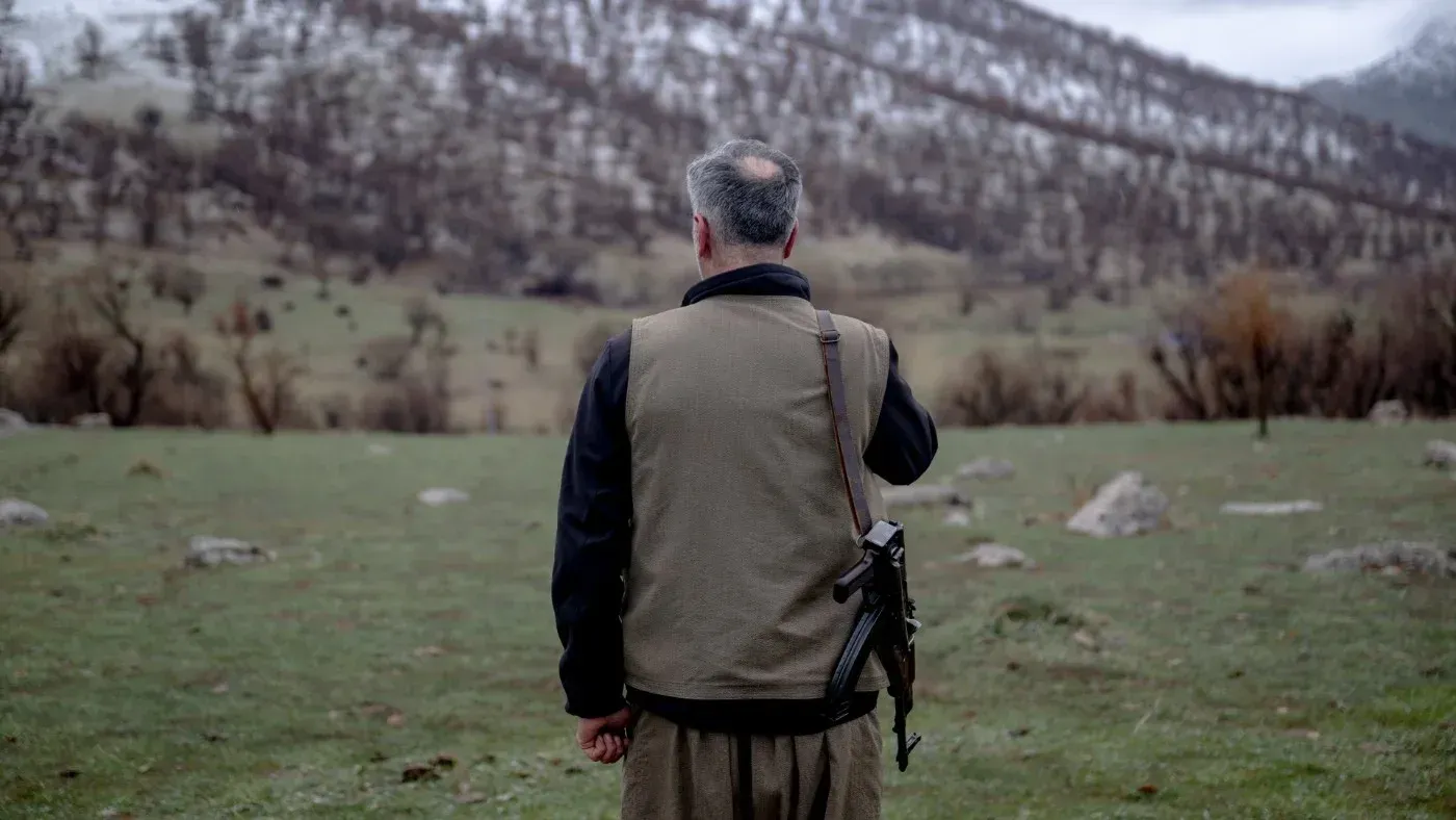 رجل مسلح يقف في منطقة جبلية، يراقب الأفق، مما يعكس التوترات المتزايدة بين الجماعات الكردية وإيران في ظل الصراع الإقليمي.